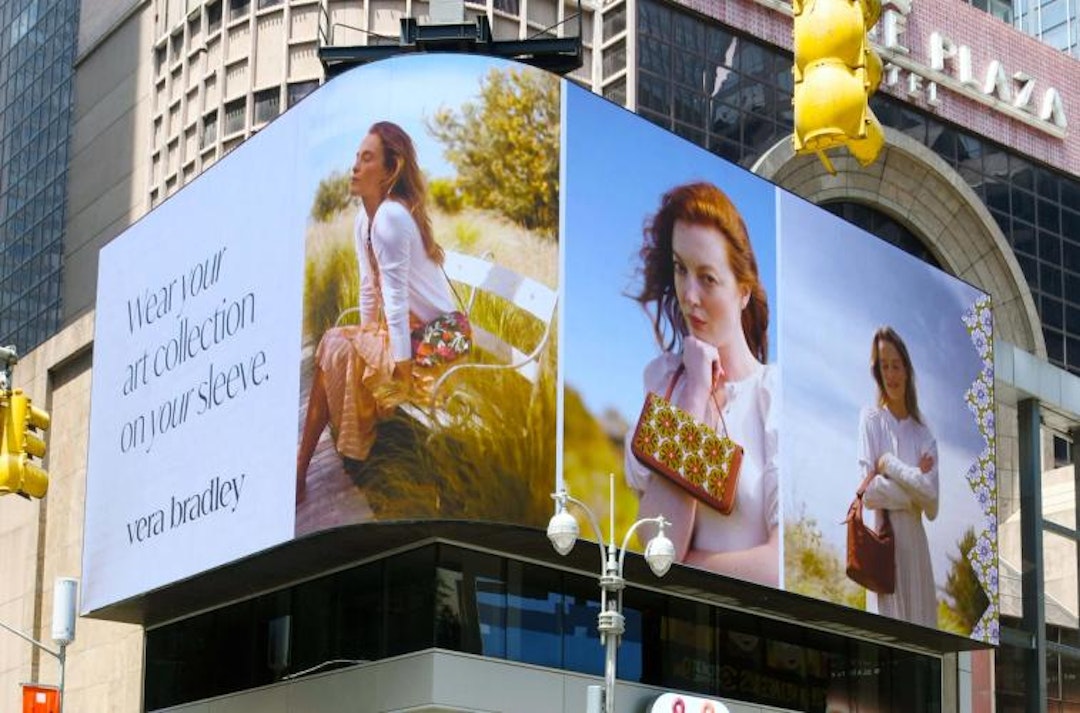 Billboard advertisement for Vera Bradley showcasing three women in outdoor settings, each featuring different handbags. The text on the left reads 'Wear your art collection on your sleeve.' The background highlights a sunny, natural environment, emphasizing the brand's focus on artistic and nature-inspired designs.